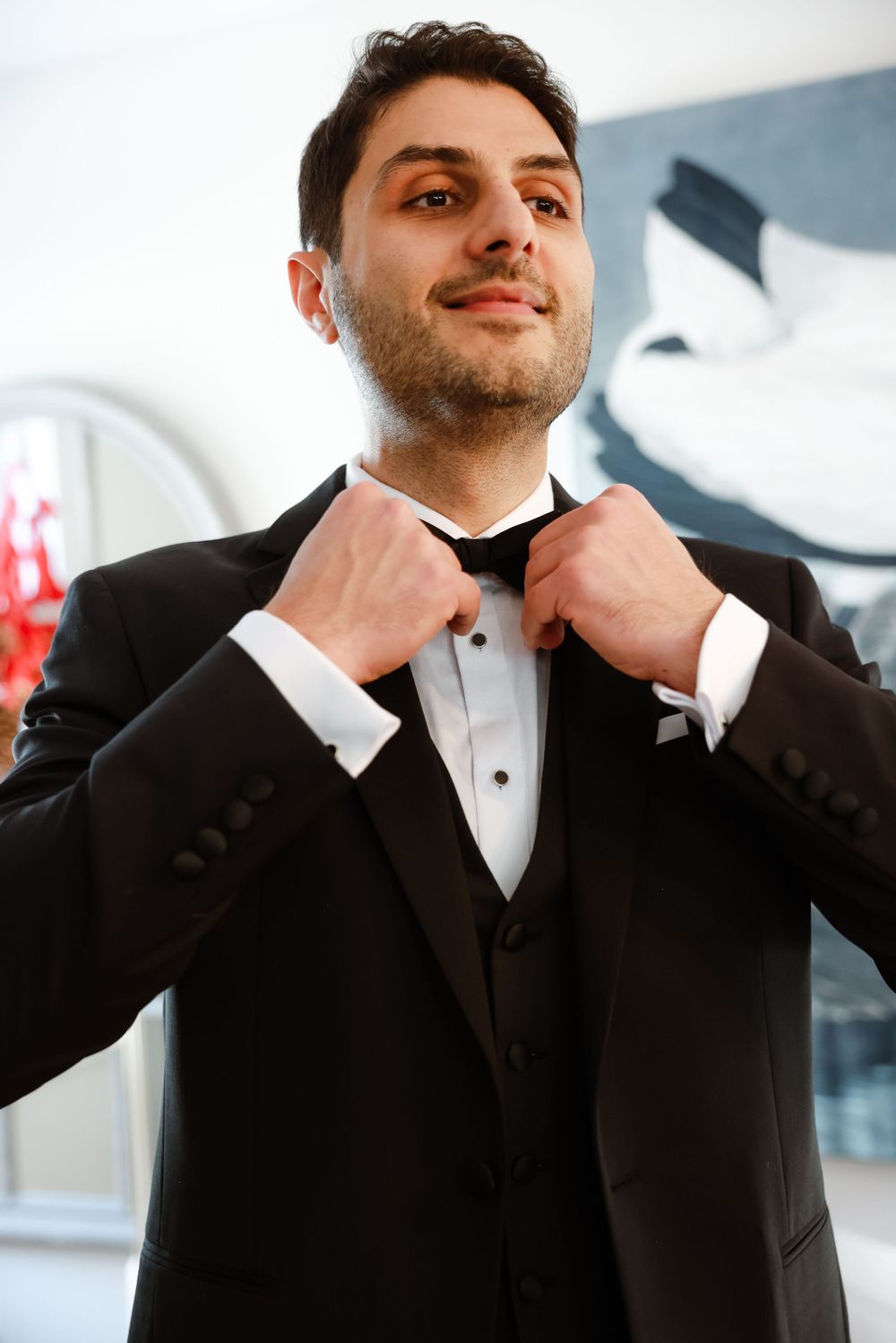 A well-dressed person adjusts their bow tie while wearing a formal black tuxedo.