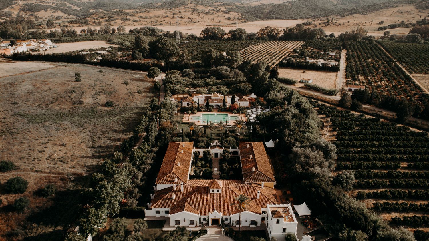 Aerial view of Spanish colonial mission estate surrounded by vineyards and orchards in California countryside.