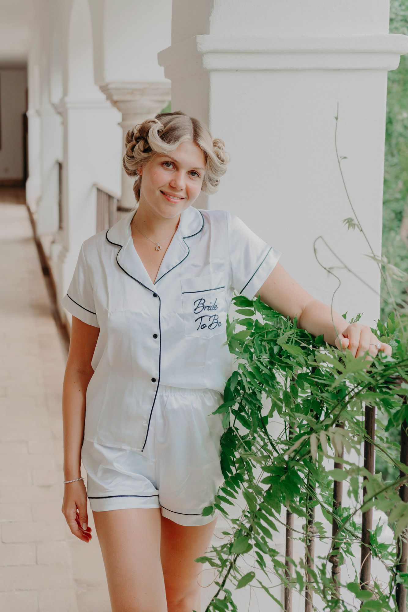 Vintage-inspired white pajama set with navy piping trim and embroidered monogram detail, shown on a sunlit porch.