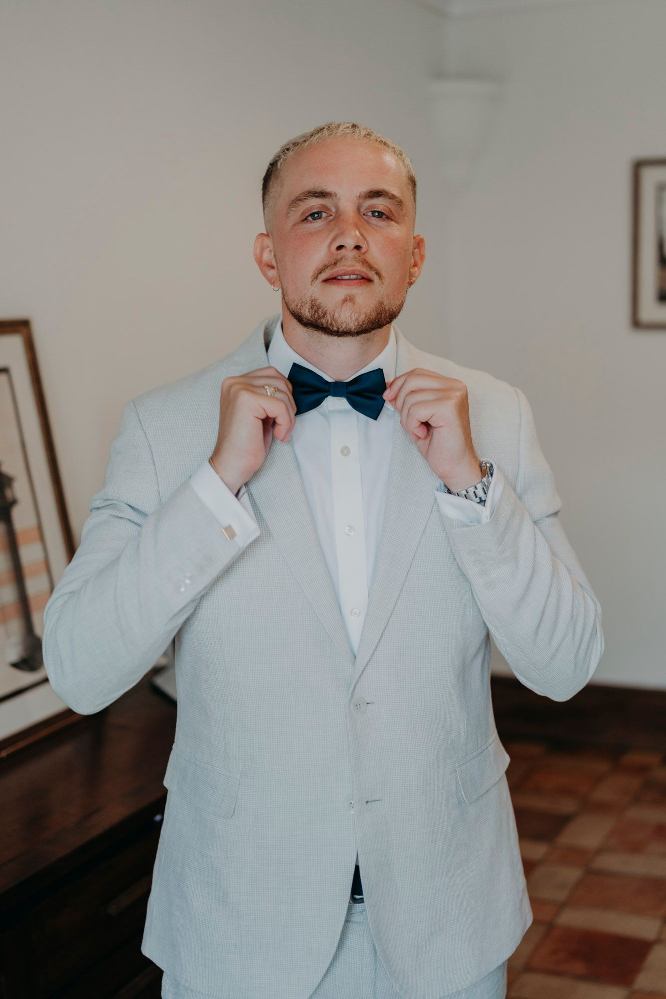 A person in a white tuxedo jacket and bow tie adjusts their formal attire while getting ready for a special occasion.