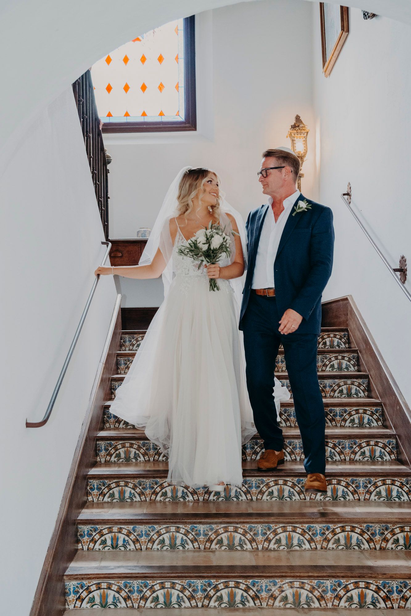 Couple standing on ornate tiled stairs during a wedding photoshoot in formal attire.
