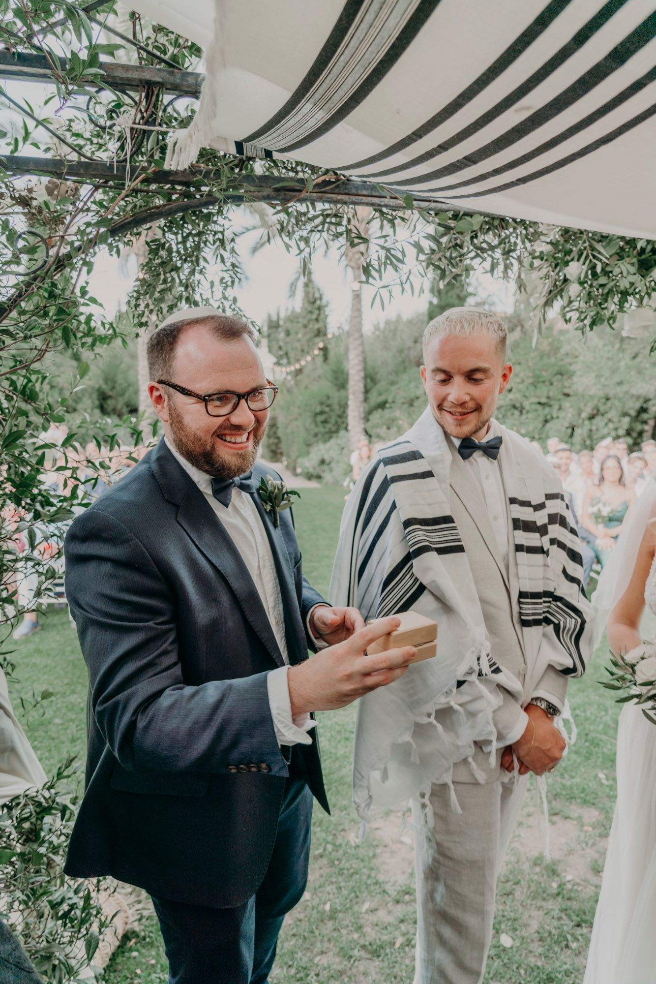Two people share a joyful moment under a draped wedding canopy decorated with greenery during an outdoor ceremony.
