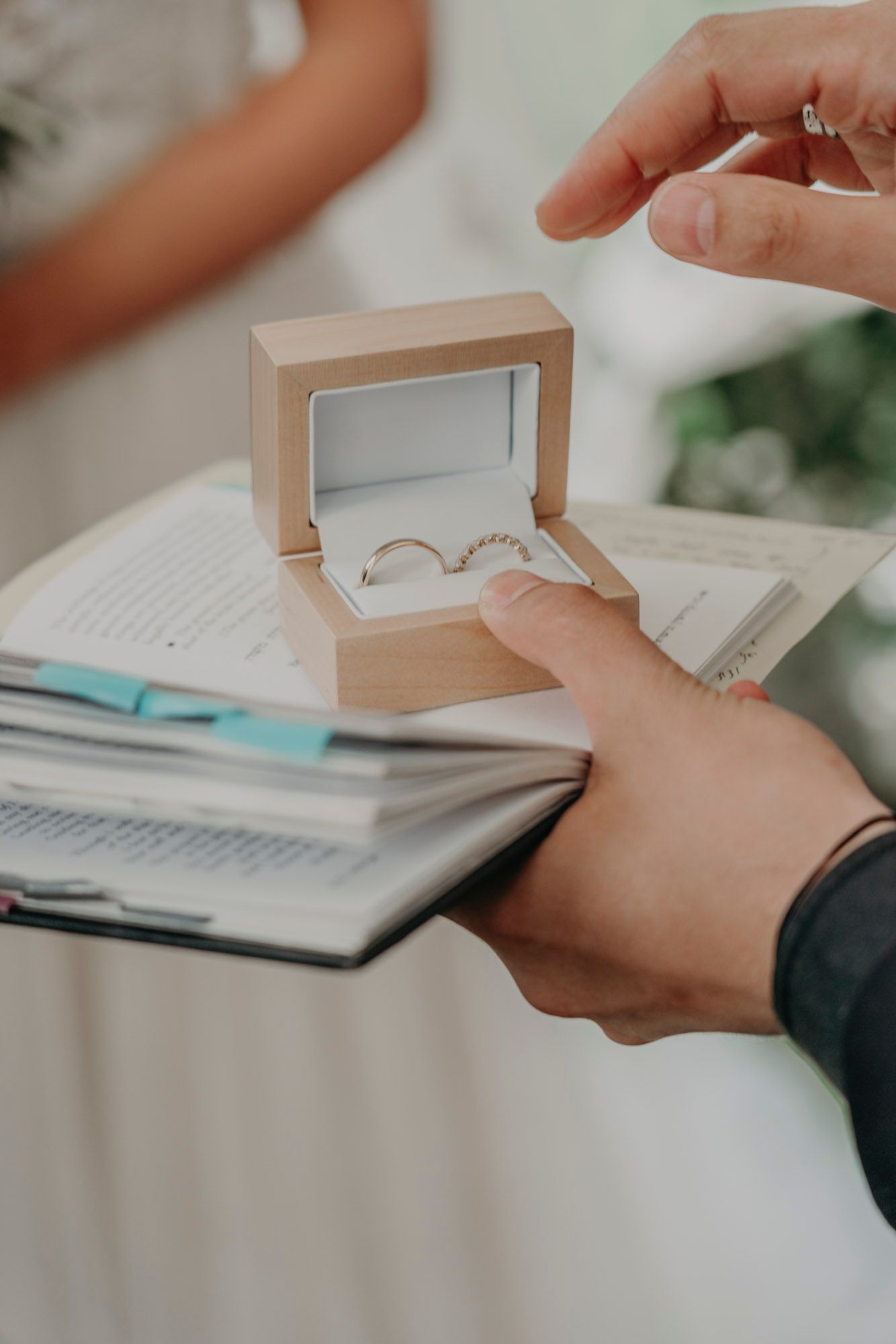 Close-up shot of hands opening a wooden ring box with wedding bands on paperwork.