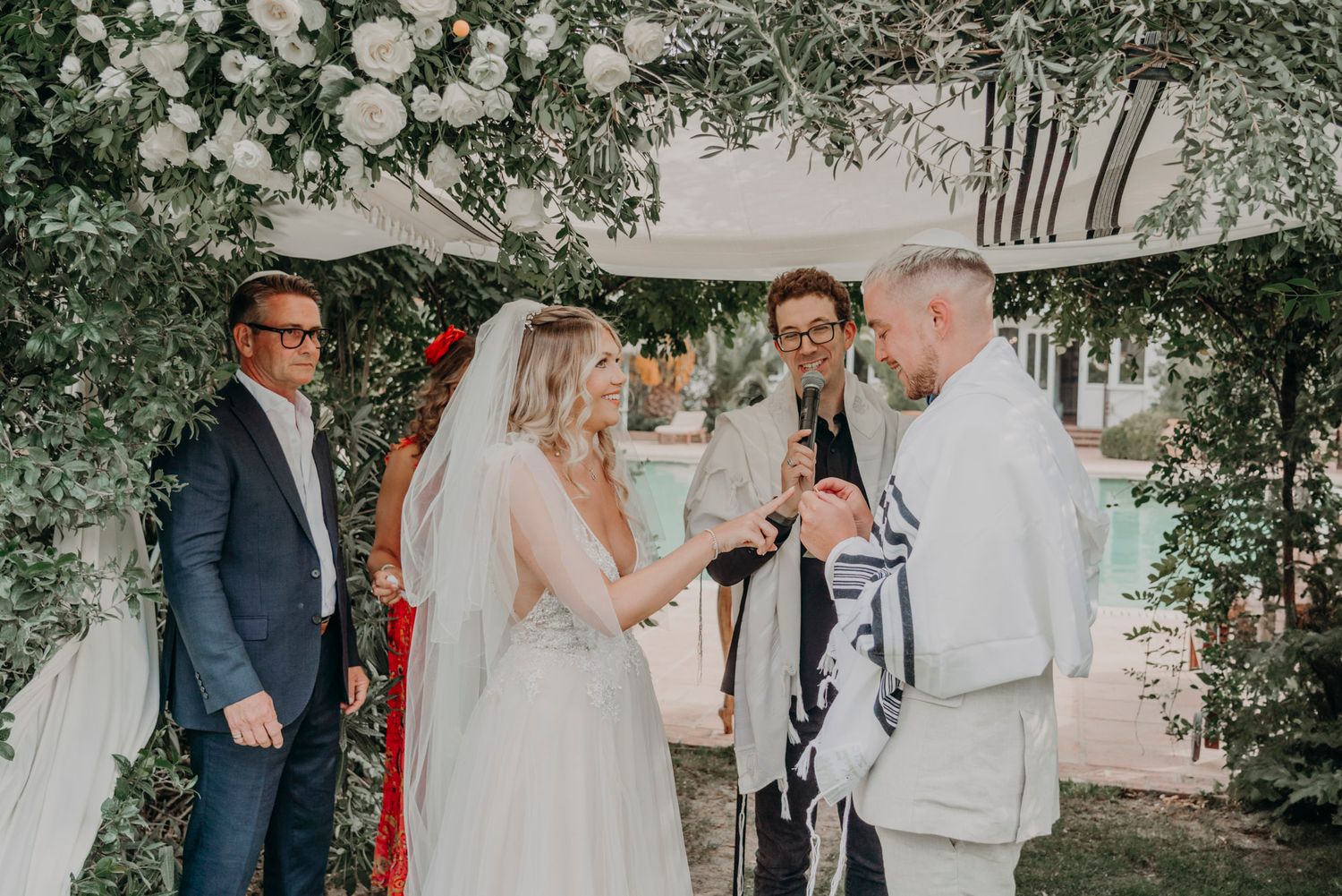 Wedding ceremony under a floral arch with white roses and greenery decorations.