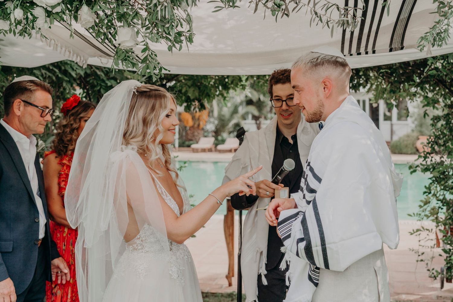 Intimate wedding ceremony moment under a decorated archway beside a swimming pool.