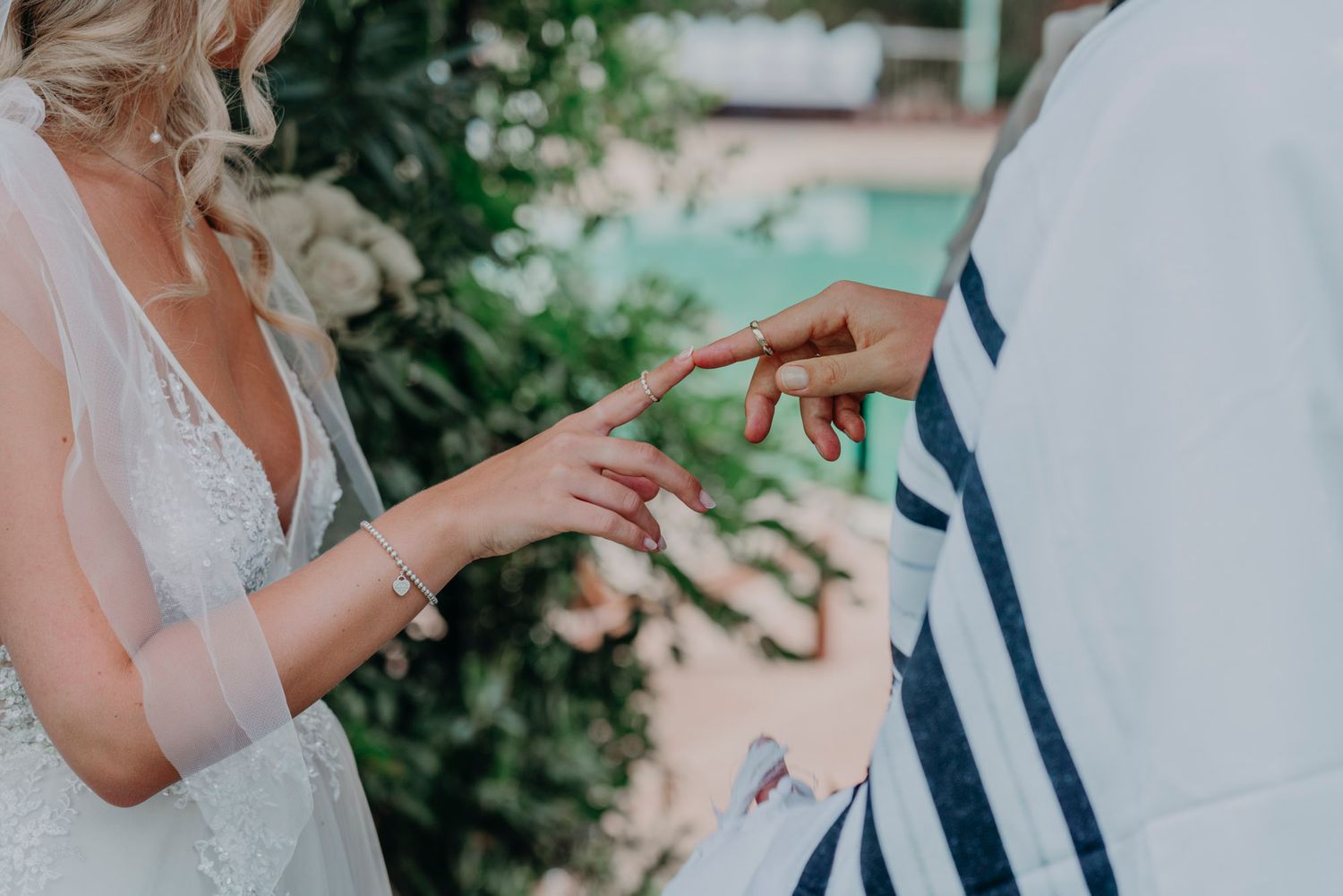 A close-up shot of hands exchanging wedding rings during an outdoor ceremony with greenery in the background.