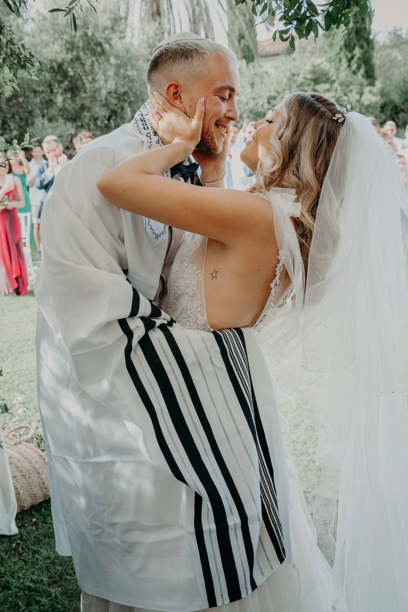 Beautiful tender moment between newlyweds dancing outdoors at their wedding ceremony while guests look on in background.