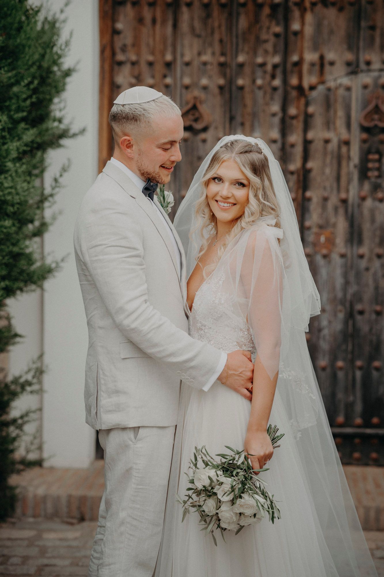 Elegant newlywed couple sharing romantic moment in front of rustic wooden door during outdoor wedding shoot.