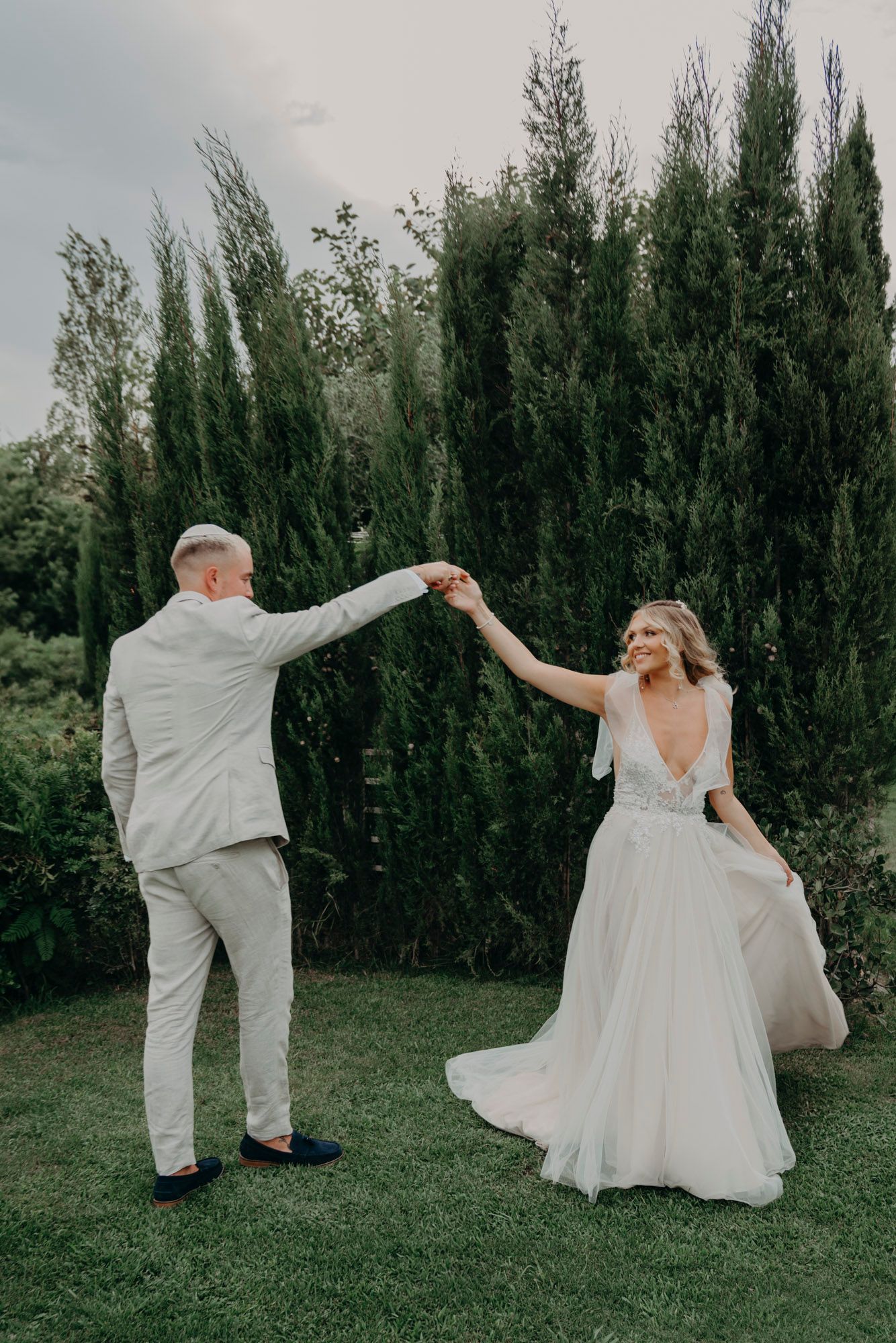 A couple dancing together on a lawn with tall cypress trees in the background during a romantic outdoor celebration.