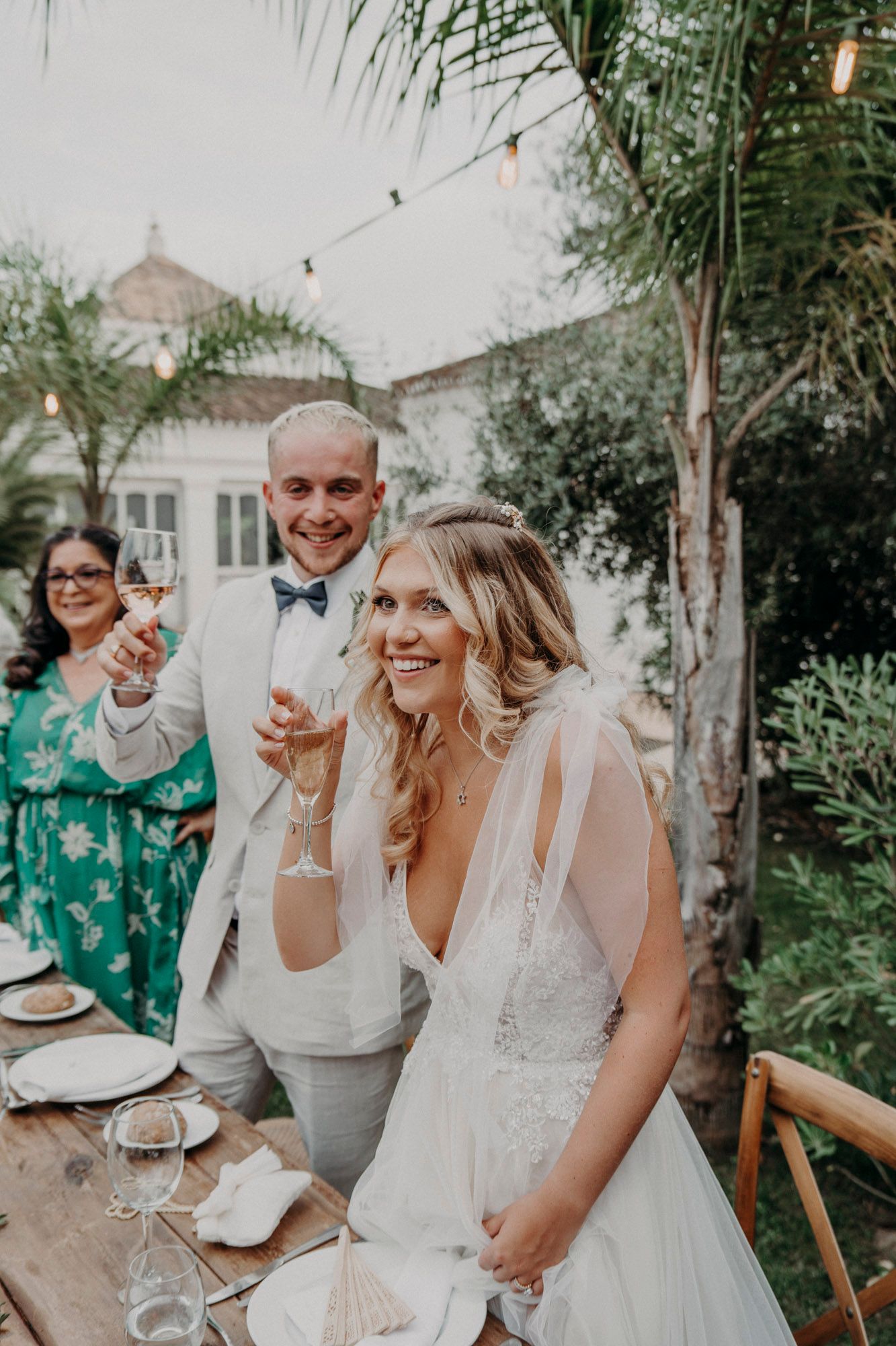 People celebrate with champagne at an outdoor garden wedding reception with string lights and palm trees.