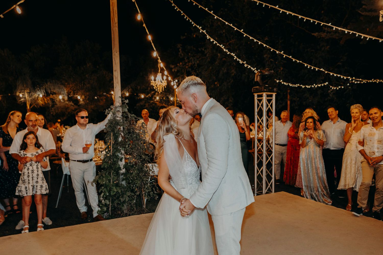 A romantic dance moment under glowing string lights at an outdoor evening wedding reception.