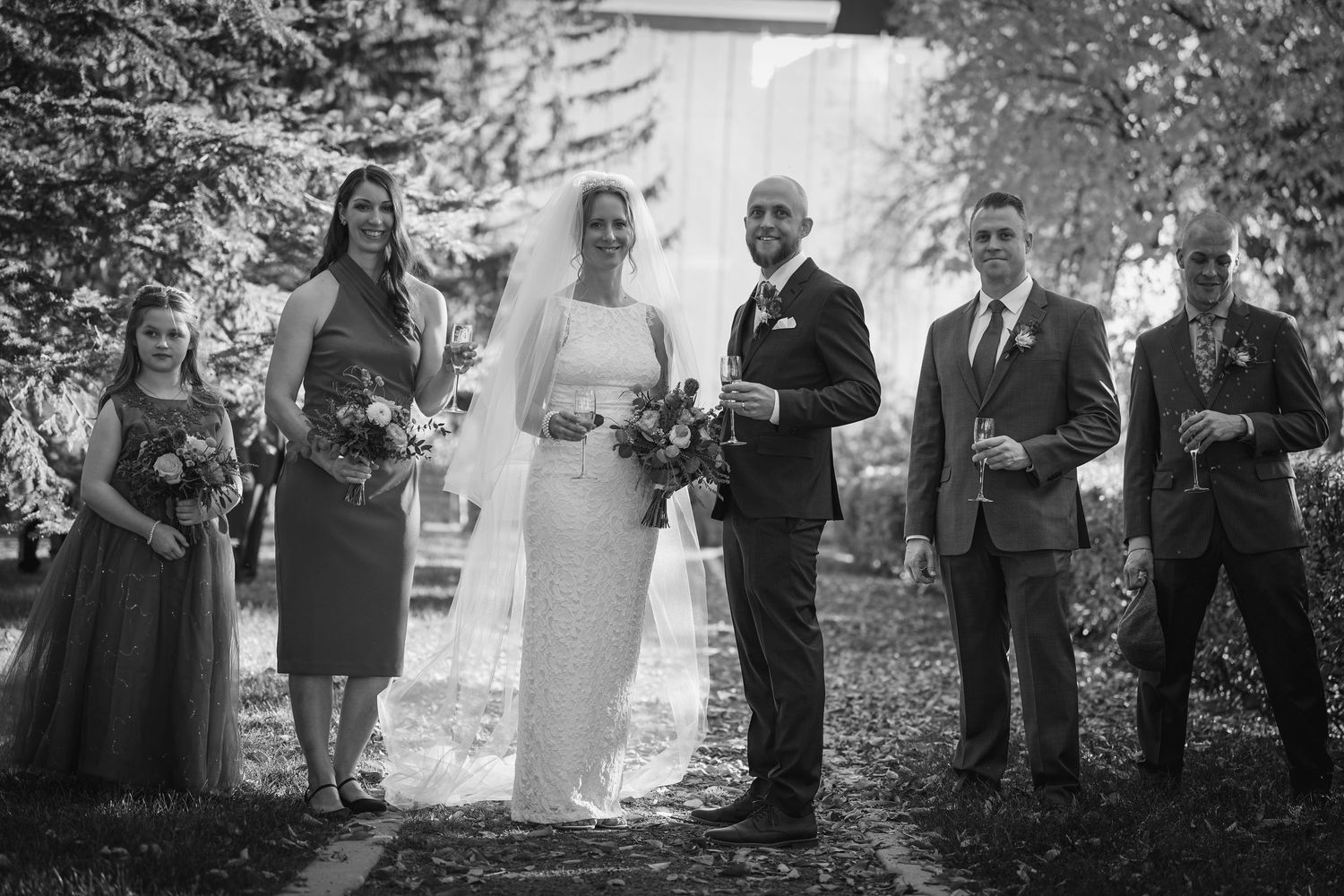 Wedding party lined up outdoors in formal attire for black and white photograph.