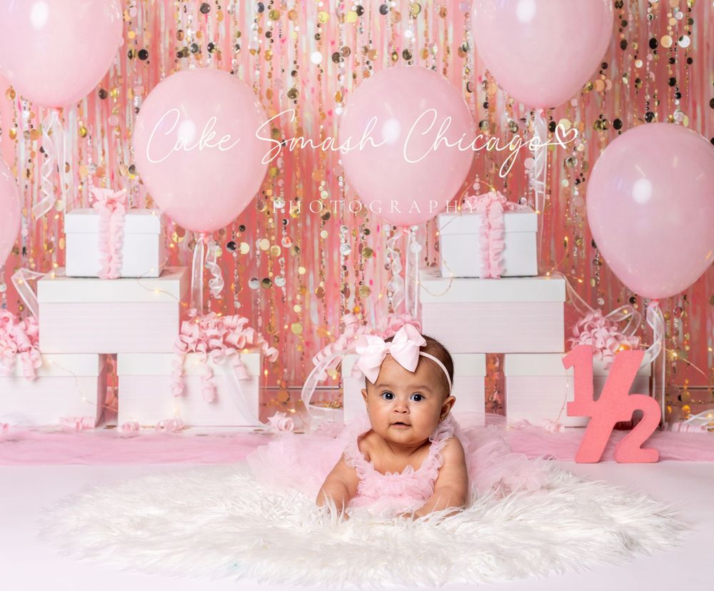 Baby celebrating half a birthday-themed cake smash in Glenview IL studio with pink decor, balloons, and playful setup.