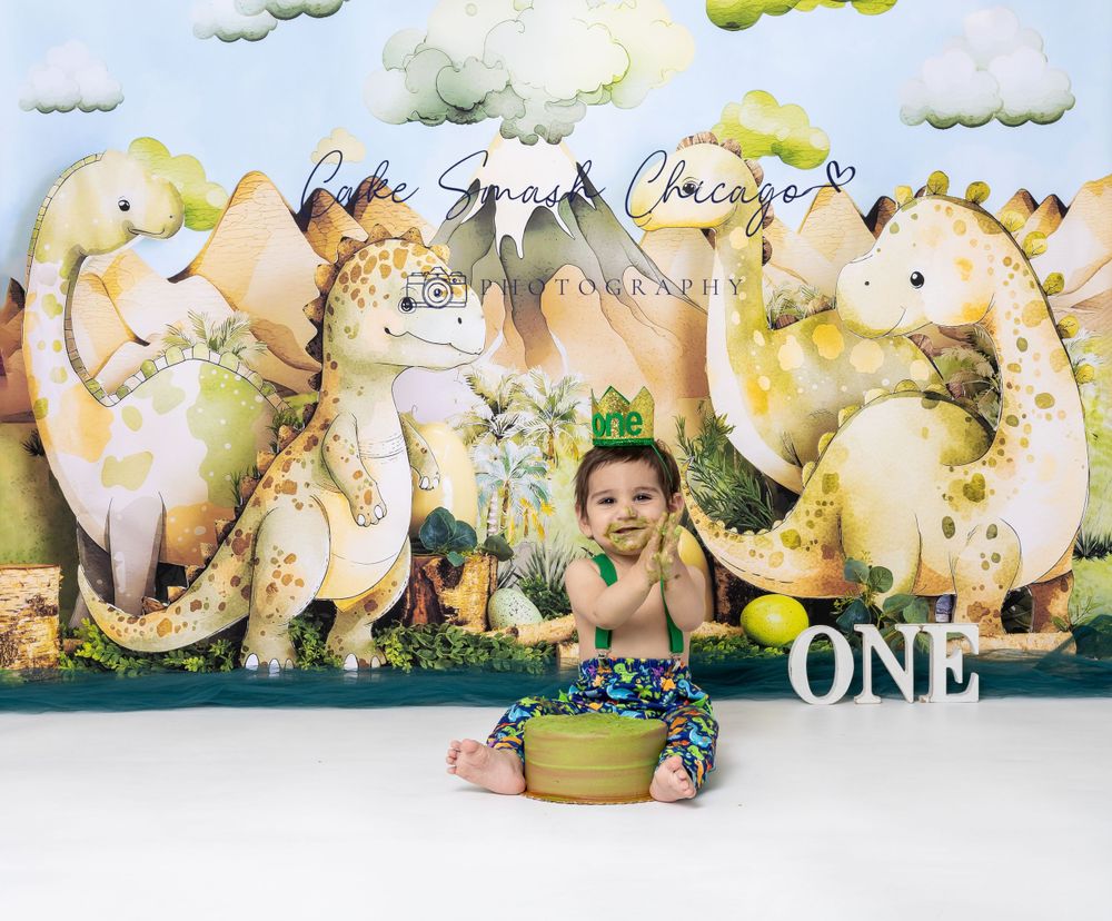 Baby during One-a-Saurus dinosaur-themed cake smash in Glenview IL studio with dinosaur backdrop, greenery, and fun props for first birthday