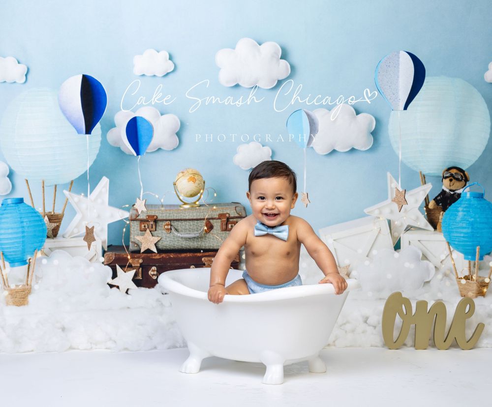 Baby during One Trip Around the Earth-themed cake smash in Glenview IL studio featuring hot air balloons, clouds, and travel-inspired decor.
