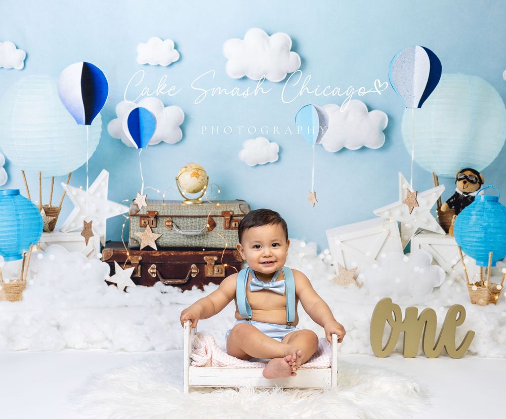Baby celebrating One Trip Around the Earth-themed cake smash in Glenview IL studio with blue skies, fluffy clouds, and adventure props.