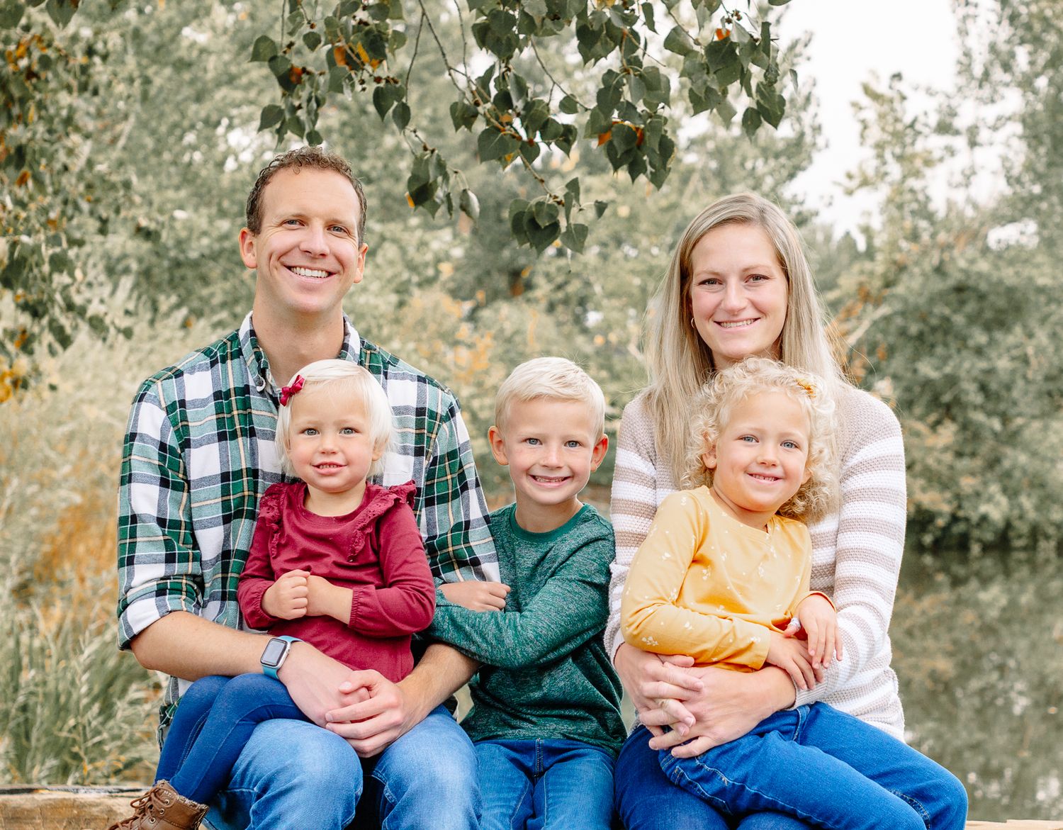 happy family of 5 sitting down smiling for their family pictures in a park in a colorado rocky mountains. 3 young kids and mom and dad.