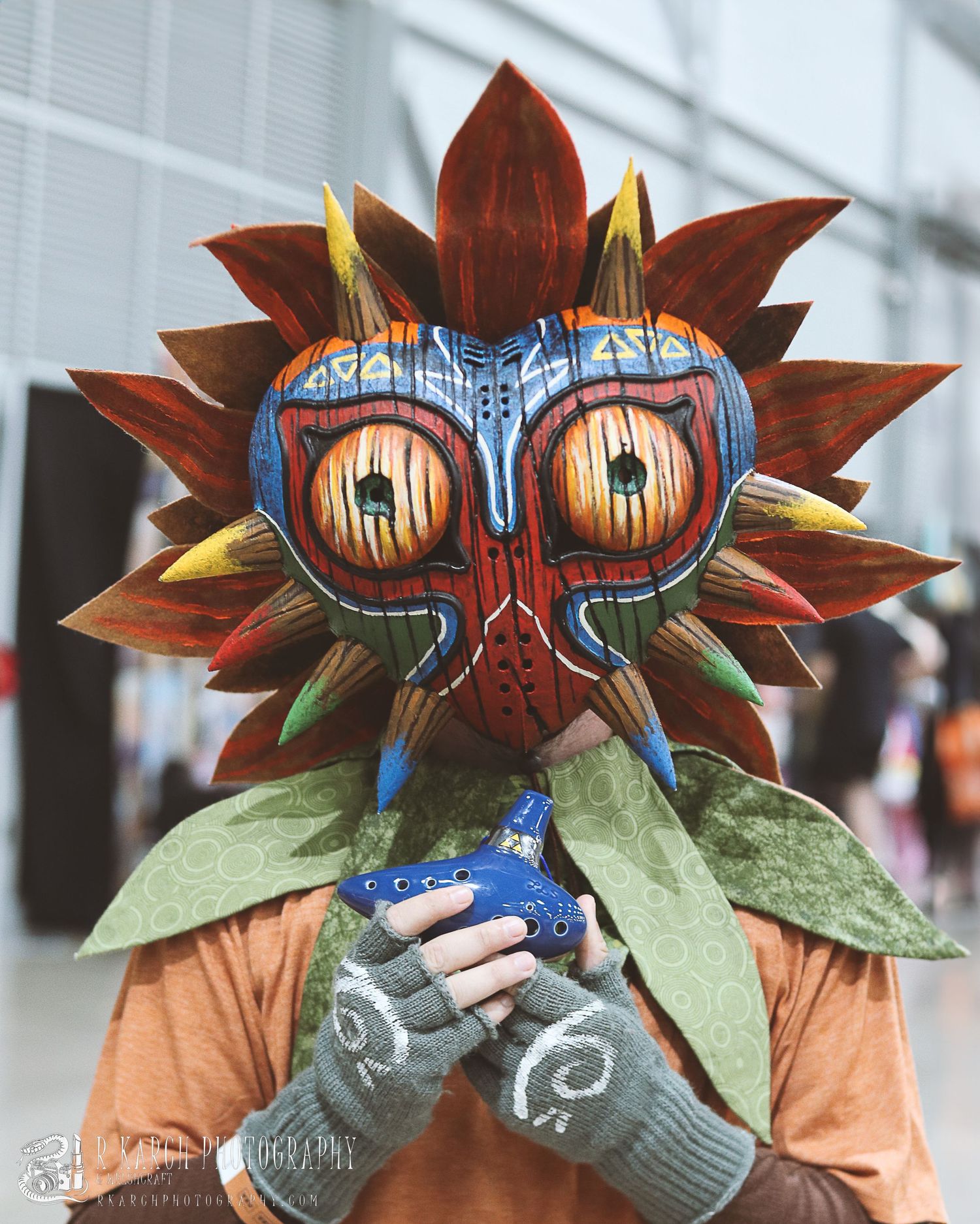 Cosplayer wearing a detailed Majora's Mask costume made with brown petals and bright blue details.