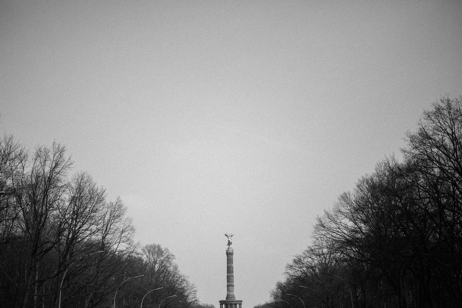 Victory Column monument in Berlin photographed from a distance between trees in black and white.
