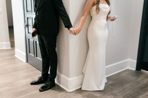 Artistic first look photo showing bride and groom holding hands around corner.