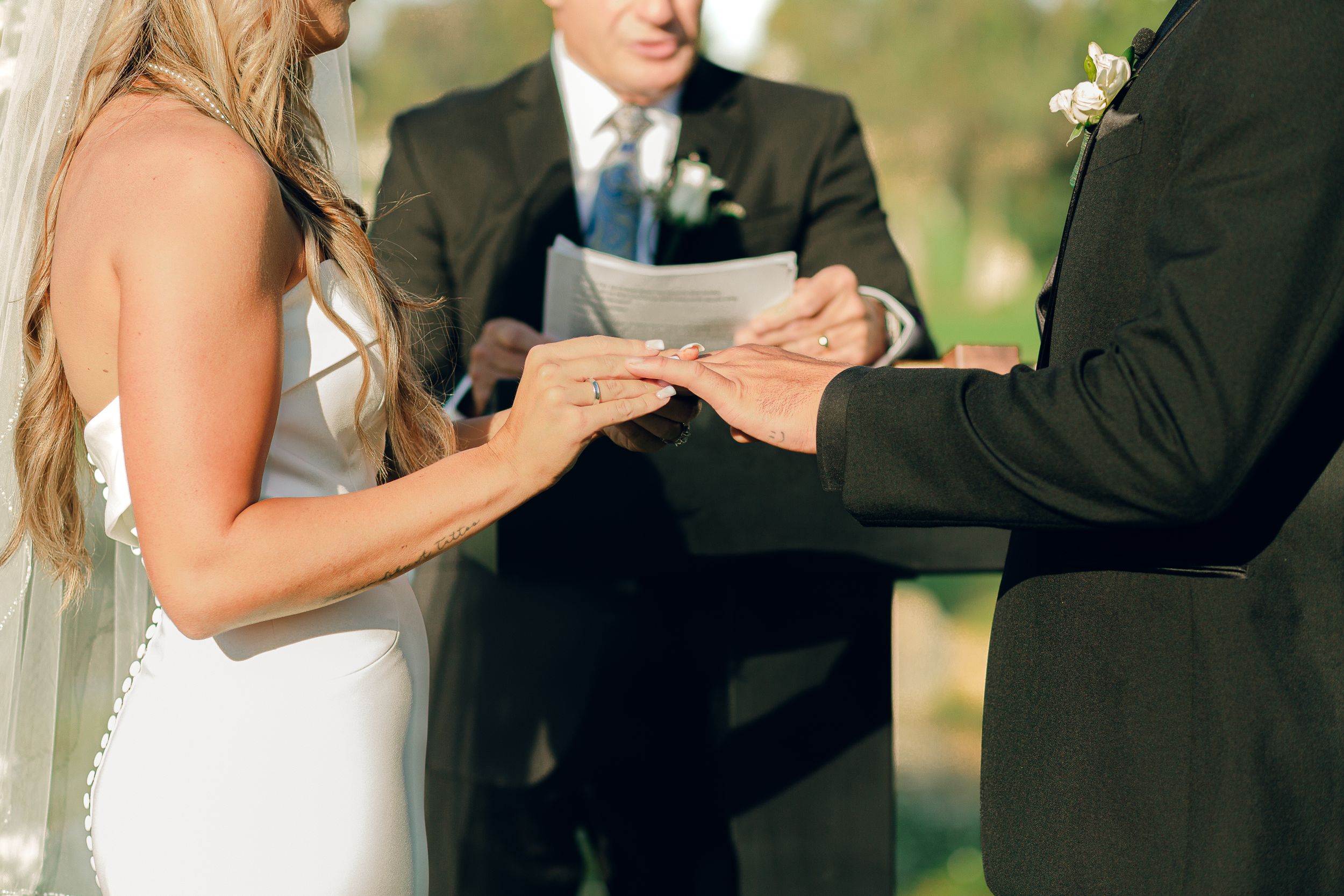 Wedding ceremony moment as couple exchanges vows outdoors with officiant holding papers.