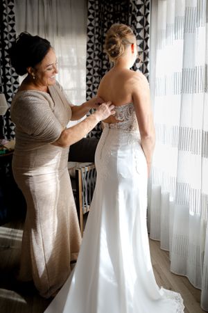 Wedding dress fitting moment captured in soft window light.