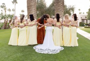 Bridal party in yellow dresses posing together on manicured lawn with palm trees.