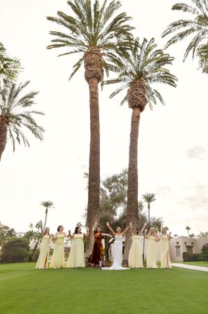 Wedding party standing beneath tall palm trees at sunset on a golf course.