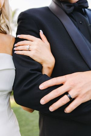 Close-up of newlyweds' hands showing wedding rings against formal attire.