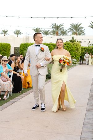 Wedding processional on outdoor pathway with palm trees and string lights.