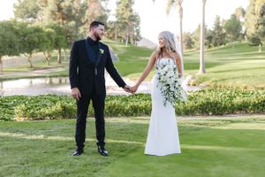 Full-length portrait of newlyweds holding hands on manicured golf course grounds.