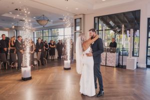 Couple shares their first dance in a bright reception venue with illuminated pillars and watching guests.
