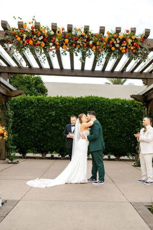 Wedding ceremony under wooden pergola decorated with orange and red flowers.