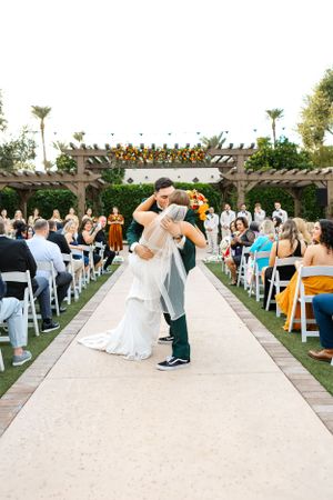 Romantic first dance at outdoor wedding ceremony under pergola decorated with orange flowers.