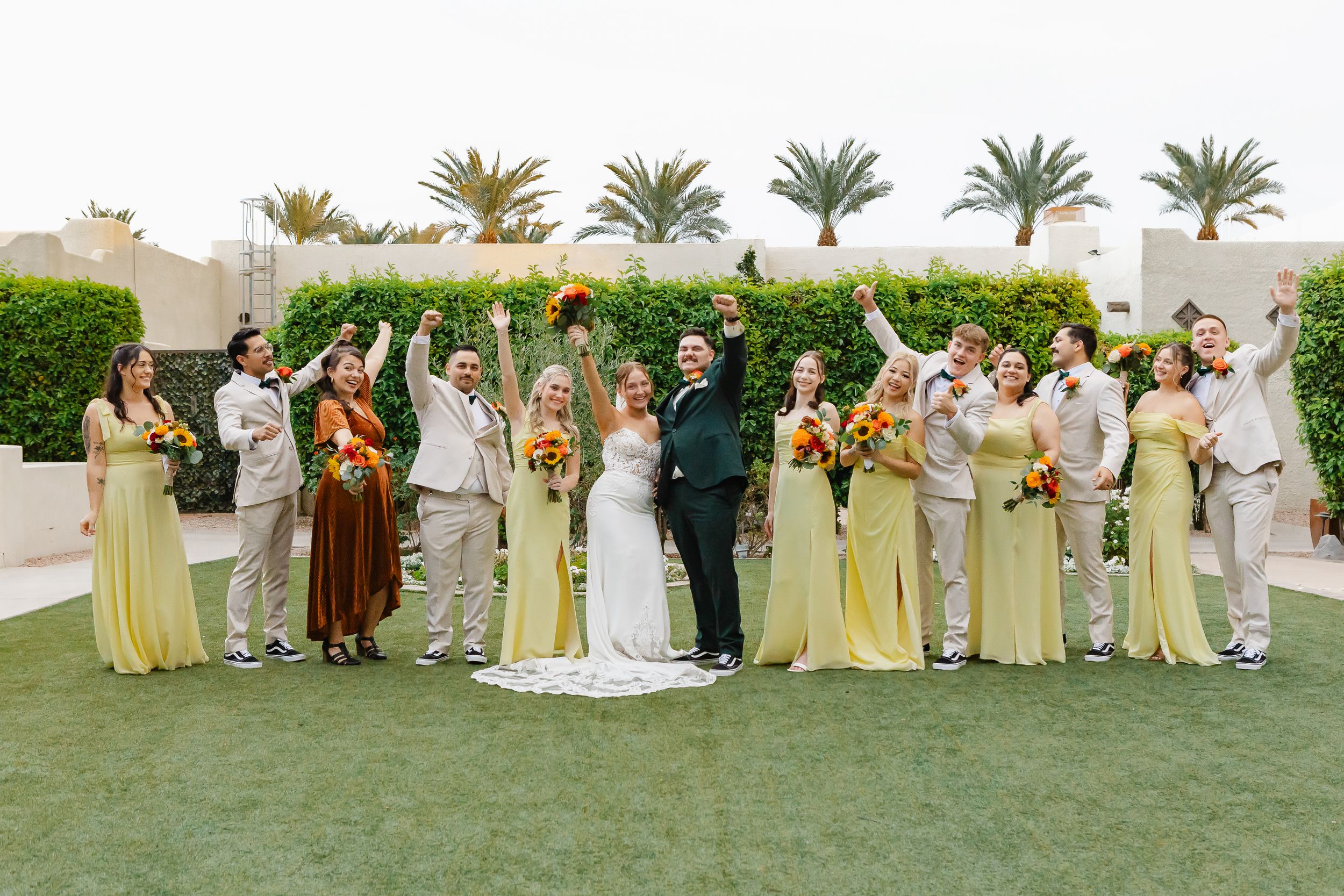 Wedding party lineup on green lawn wearing coordinated yellow and neutral formal attire.