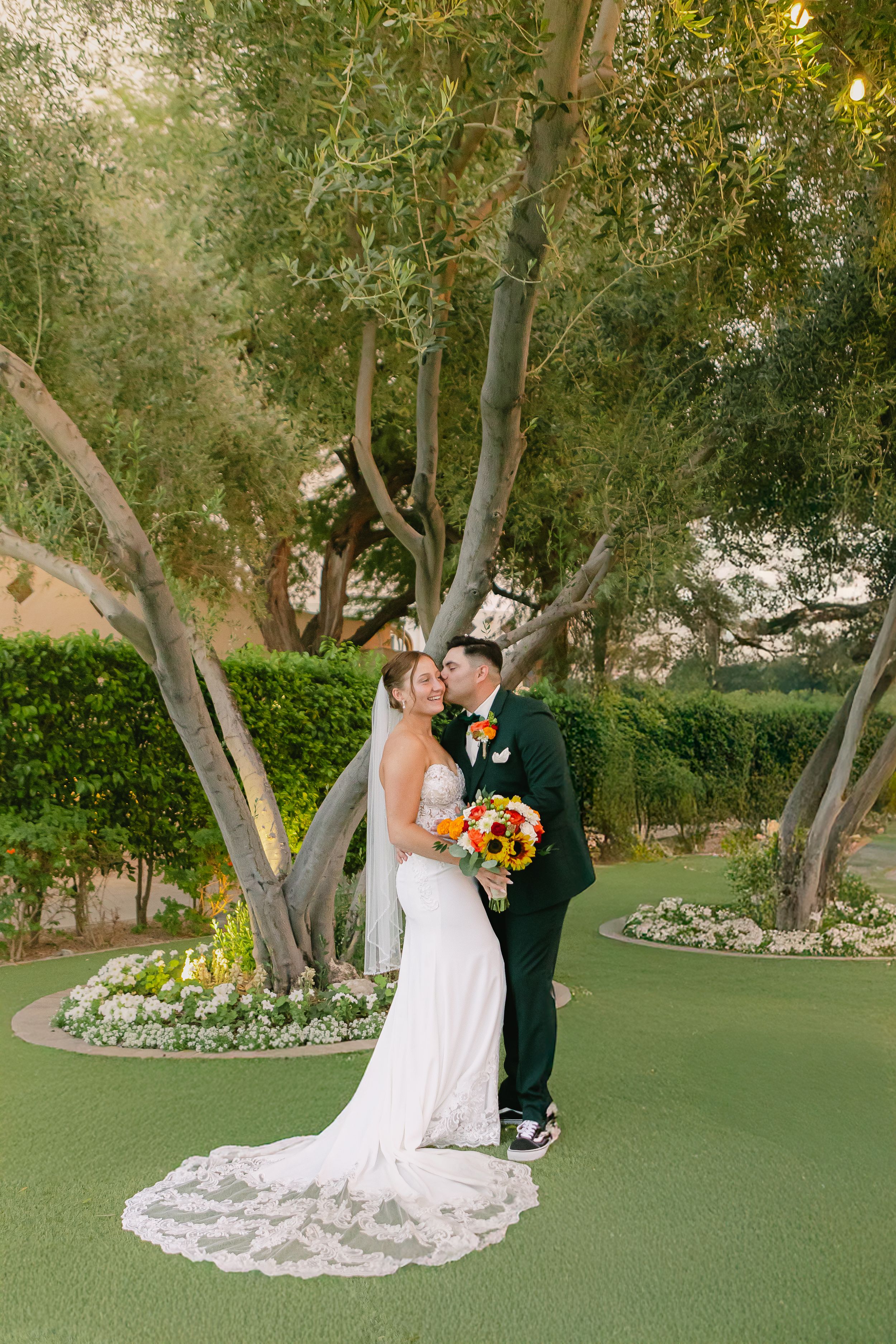 Newlyweds share romantic moment under garden trees on putting green.