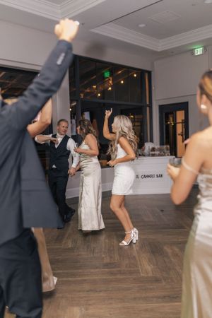Wedding party dances energetically on a hardwood floor at an indoor reception venue.