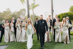 Wedding party poses on lush golf course with bridesmaids in champagne dresses and palm trees in background.