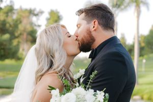 Romantic wedding couple share a kiss on a beautiful golf course with palm trees.