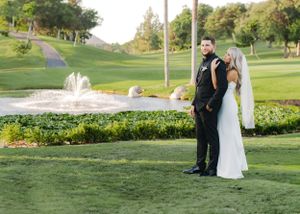 Wedding couple poses by fountain on elegant golf course surrounded by landscaped gardens.