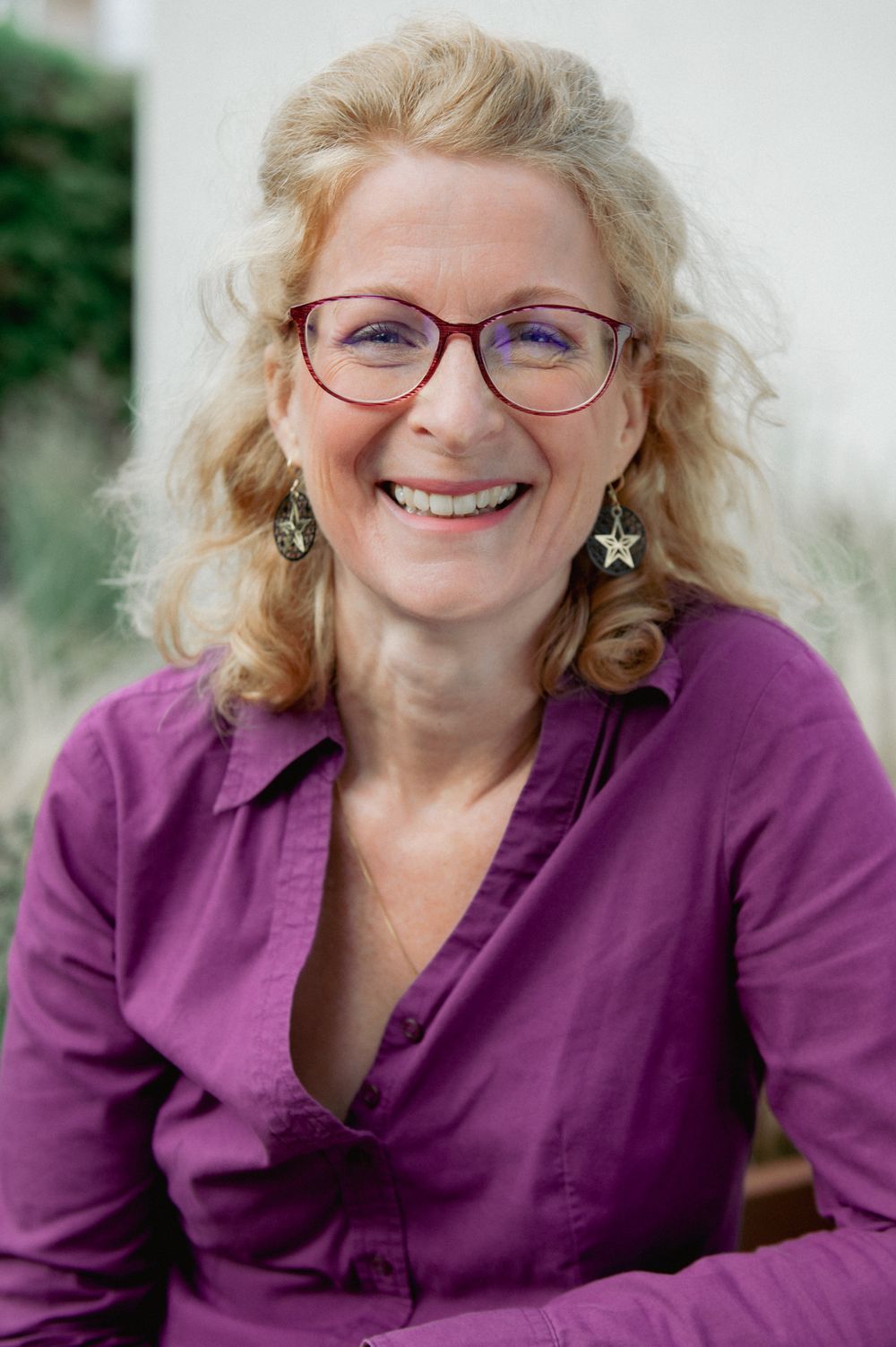 Professional headshots of someone wearing a purple button-down shirt against natural background.