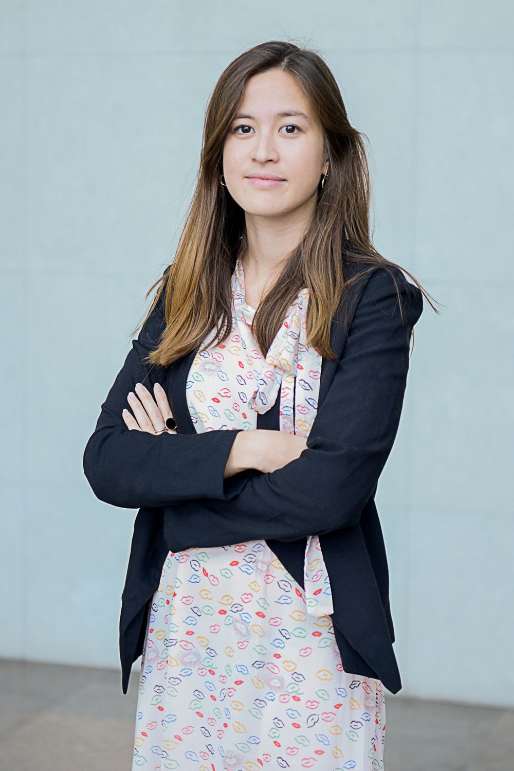 Person in floral dress and navy blazer poses against neutral wall.