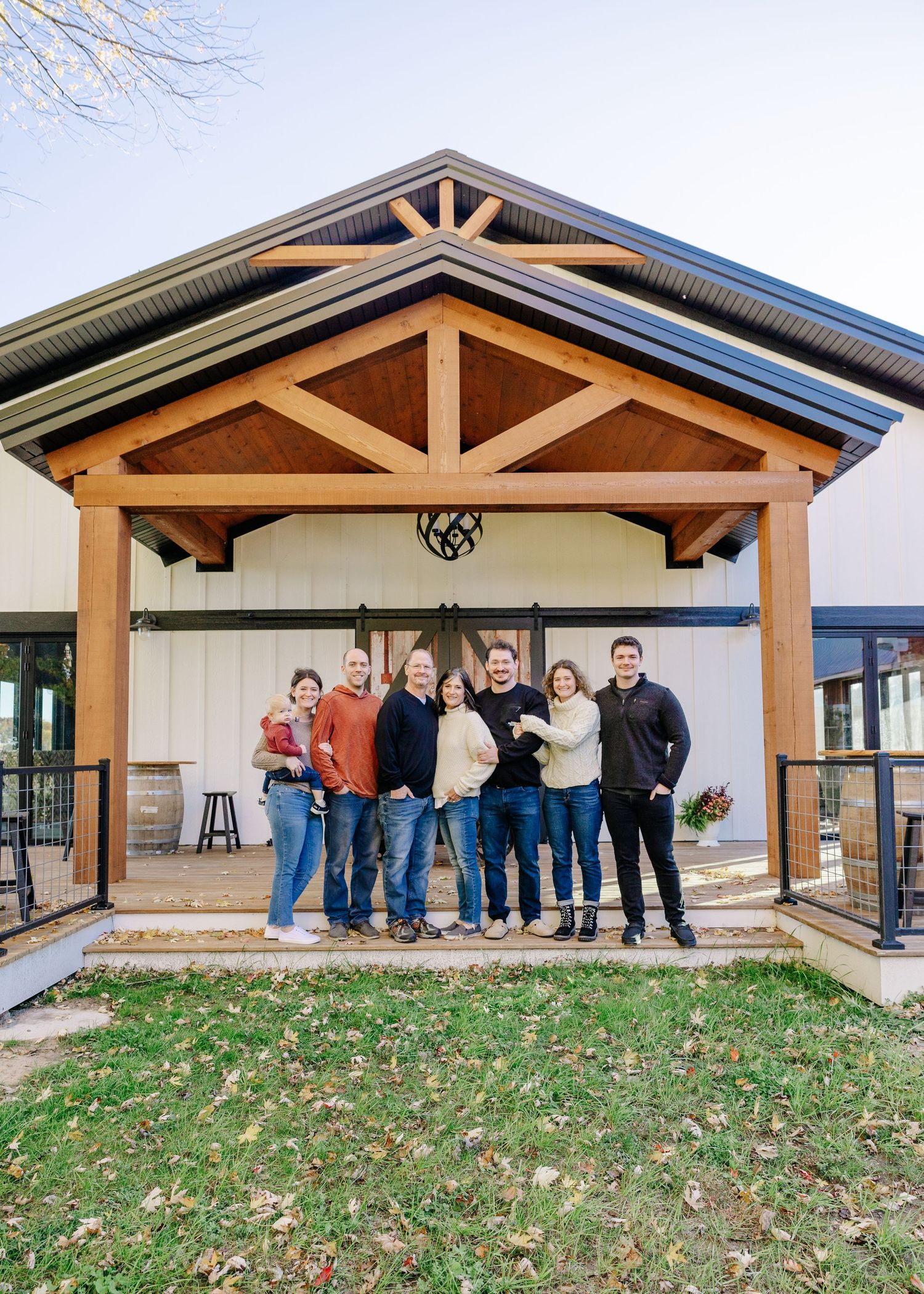 An extended family photoshoot poses together on a wooden porch with rustic timber frame architectural details in Minnesota.