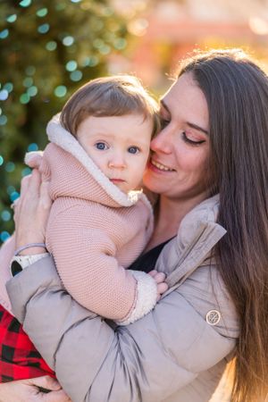 Parent holding and smiling at baby wearing pink sweater against bokeh background.