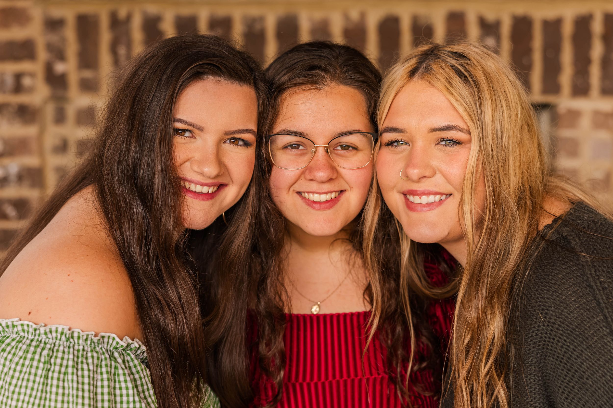 Three friends share laughter together against brick background.
