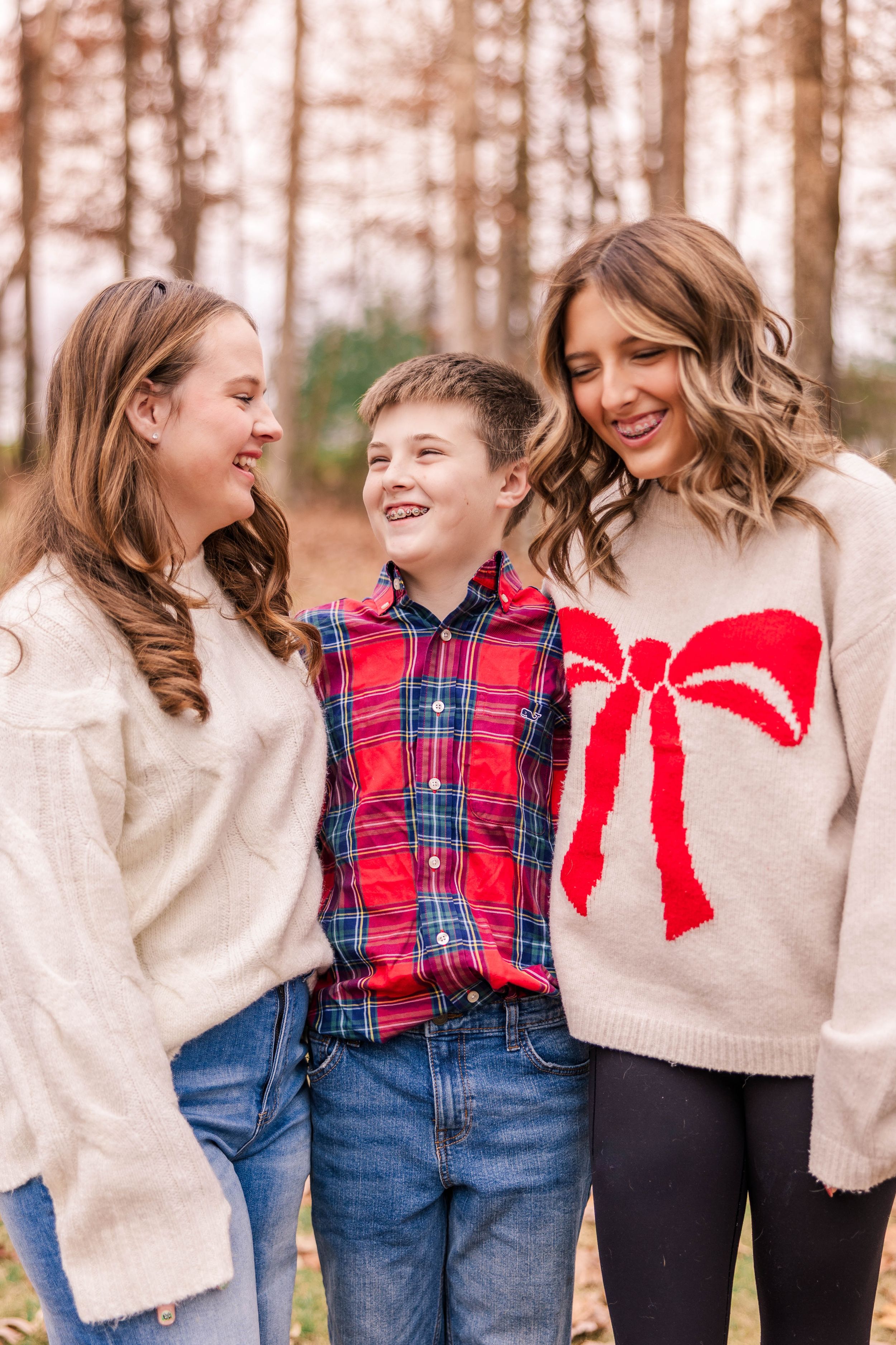Three people in warm winter sweaters share a joyful moment together in a forest setting with fall foliage.