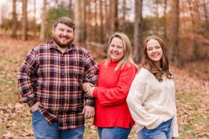A casual group photo outdoors with people wearing plaid and knit sweaters against an autumn forest backdrop.