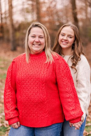 Two people pose together outdoors, wearing a bright red cable knit sweater and white sweater.