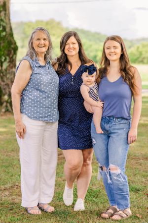 Three generations pose together outdoors in casual clothing on a sunny day.