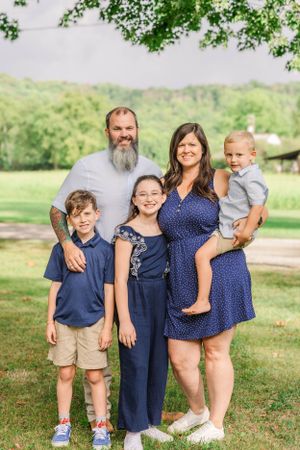 Family of five poses together outdoors with scenic rolling hills in background.